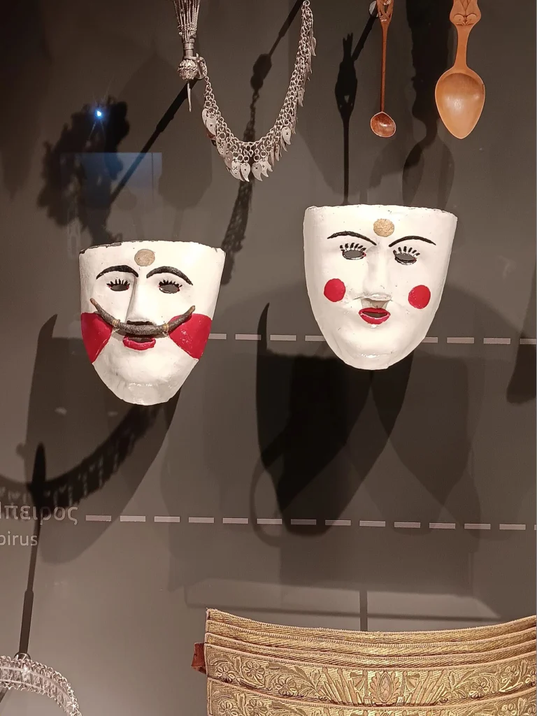 Δύο λευκές προσωπίδες, ανδρική με μουστάκι και γυναικεία με κόκκινα μάγουλα, από το έθιμο της Νάουσας