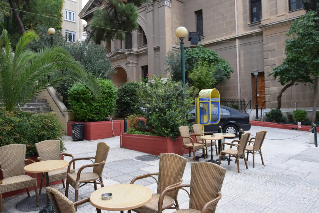 Ψάθινες πολυθρόνες και στρογγυλά τραπεζάκια καφέ σε πλακόστρωτη αυλή με φυτά στο Κολωνάκι