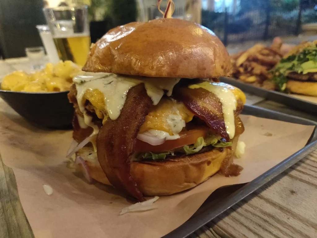 Μεγάλο burger εστιατορίου με τηγανητό κοτόπουλο, μπέικον, λιωμένο τυρί και σάλτσα σε μεταλλικό δίσκο