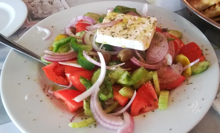 Χωριάτικη σαλάτα με ντομάτα, αγγούρι, κόκκινο κρεμμύδι, πιπεριά, ελιές και κομμάτι φέτα με ρίγανη σε άσπρο πιάτο