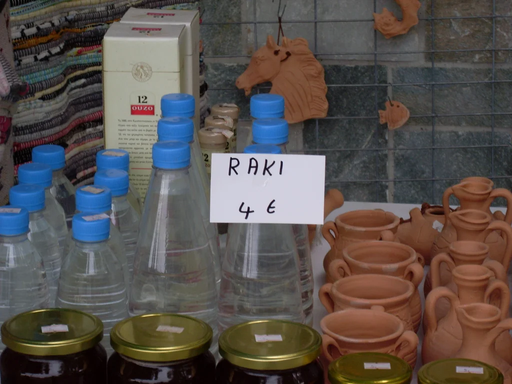 Χύμα ρακή σε πλαστικά μπουκάλια με χειρόγραφη ταμπέλα, δίπλα σε πήλινα σε πάγκο πώλησης
