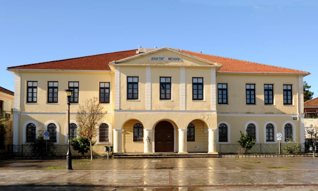 Η κίτρινη νεοκλασική πρόσοψη του Δικαστικού Μεγάρου της Πρέβεζας με τοξωτή είσοδο και κεραμοσκεπή