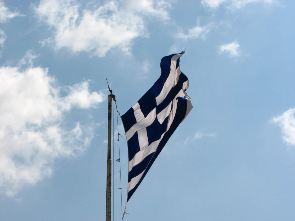 Ελληνική σημαία κυματίζει σε ιστό κάτω από γαλάζιο ουρανό με λευκά σύννεφα