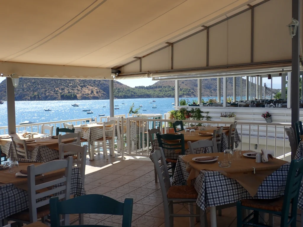 Άδεια τραπέζια με καρό τραπεζομάντιλα σε σκεπαστή βεράντα εστιατορίου δίπλα στη θάλασσα στο Τολό