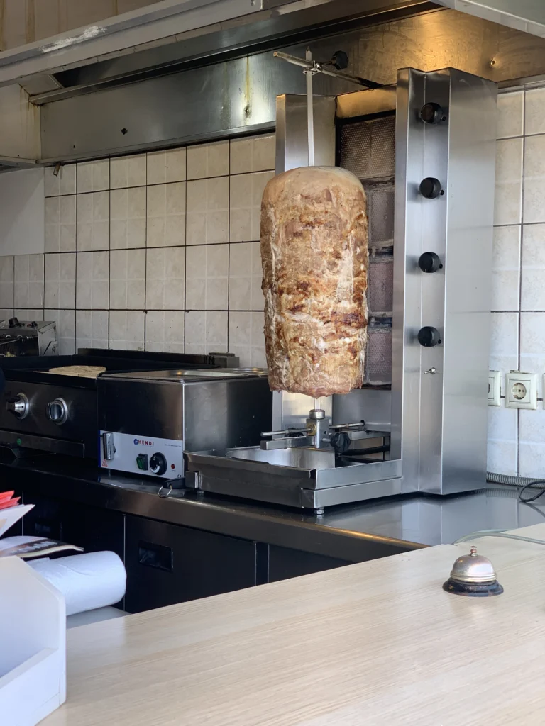 Κώνος γύρου σε κάθετη σούβλα μπροστά σε ανοξείδωτη ψησταριά με τις εστίες στο πλάι, σε κουζίνα