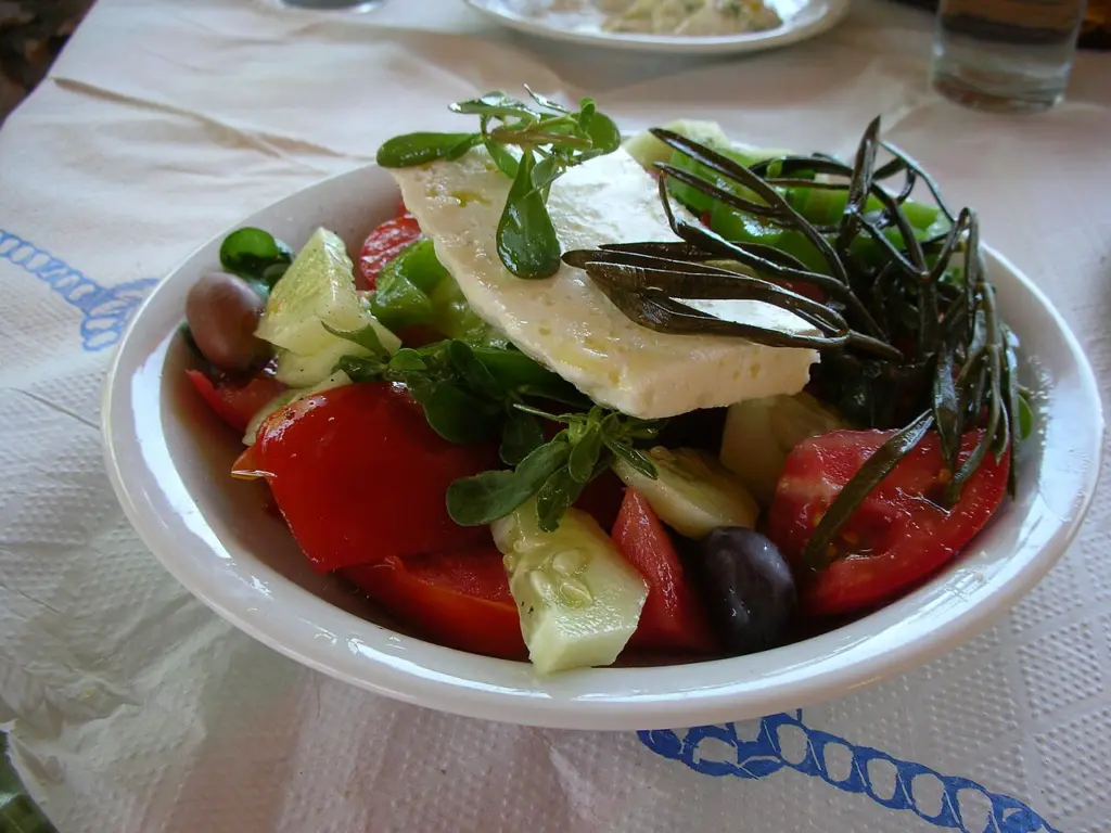 Χωριάτικη σαλάτα σε λευκό πιάτο με ντομάτα, αγγούρι, τυρί, ελιά και πράσινα φυτά, γλιστρίδα και κριθάμι