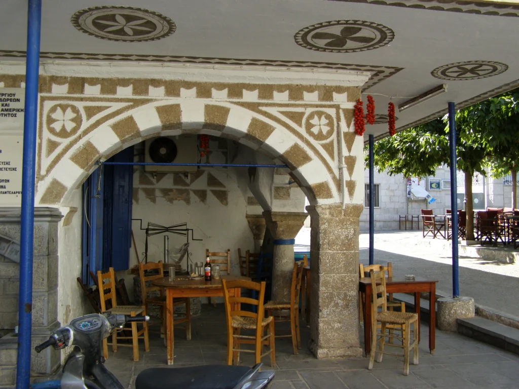 Καφενείο με ξύλινες καρέκλες κάτω από καμάρα με ξυστά σχέδια στο Πυργί της Χίου