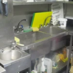 Κουζίνα μαγαζιού με νιπτήρα χεριών, διπλό ανοξείδωτο νεροχύτη και χρωματιστές επιφάνειες κοπής