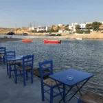 Άδεια τραπέζια ταβέρνας με μπλε καρέκλες δίπλα στη θάλασσα στο Πάνω Κουφονήσι, πριν έρθουν οι πελάτες