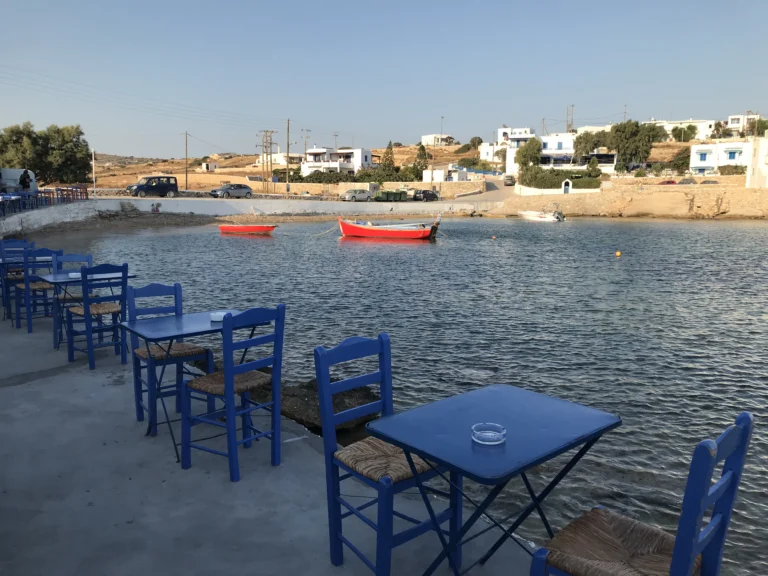Άδεια τραπέζια ταβέρνας με μπλε καρέκλες δίπλα στη θάλασσα στο Πάνω Κουφονήσι, πριν έρθουν οι πελάτες