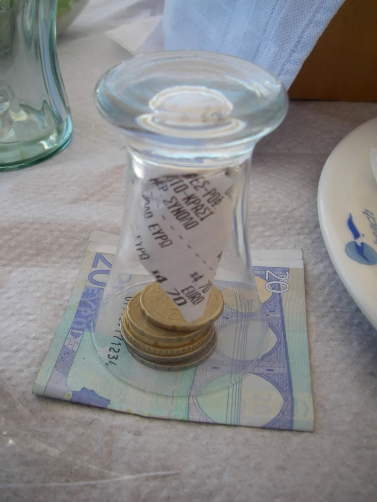 Απόδειξη λογαριασμού και κέρματα ευρώ κάτω από ανάποδο ποτήρι, πάνω σε χαρτονόμισμα των 20 ευρώ στο τραπέζι