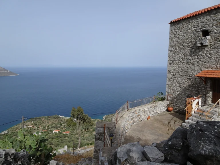 Πέτρινος πύργος της Μάνης πάνω από ελαιώνες, φραγκοσυκιές και τη θάλασσα σε καθαρή μέρα
