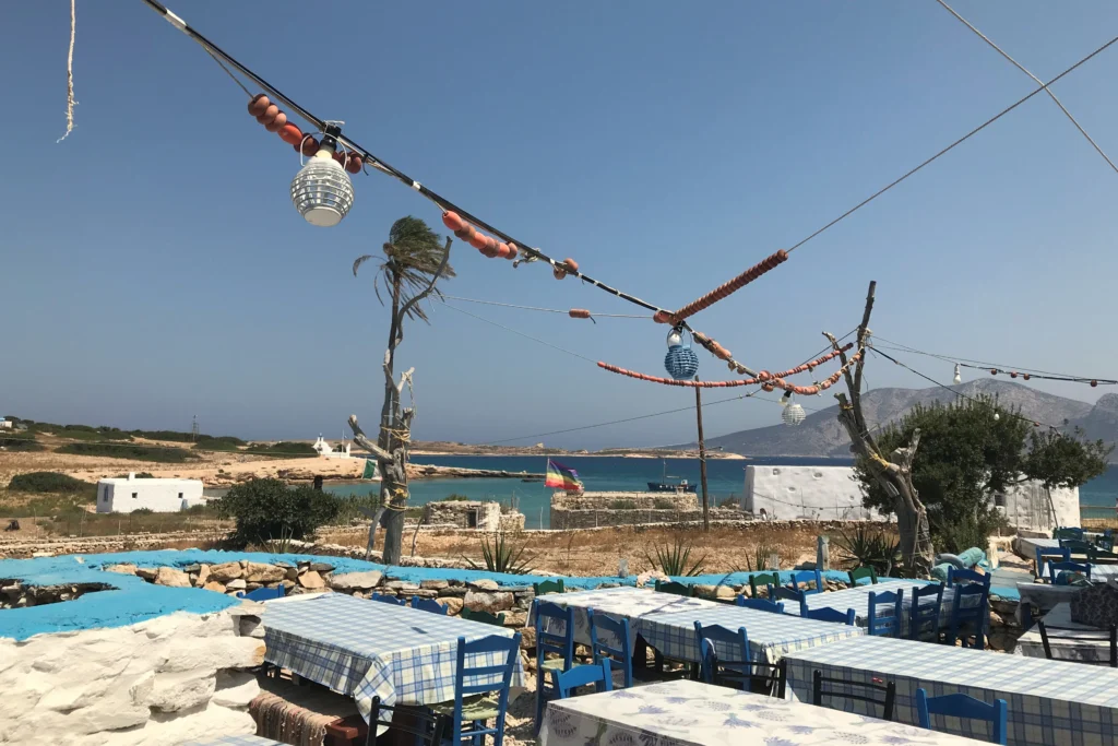 Ενωμένα τραπέζια με καρό τραπεζομάντιλα και μπλε καρέκλες σε ταβέρνα του Κάτω Κουφονησιού δίπλα στο κύμα