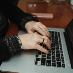 Χέρια πληκτρολογούν σε φορητό υπολογιστή πάνω σε ξύλινο τραπέζι, όπως όταν γράφεται ένας κατάλογος