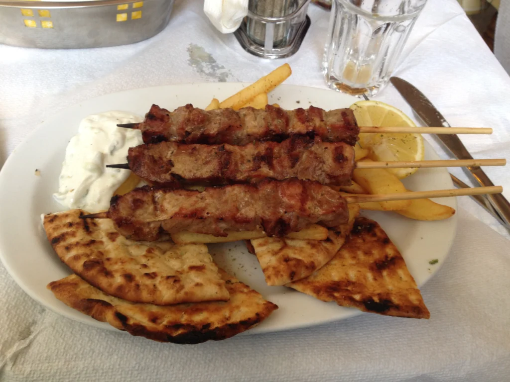 Πιάτο με τρία χοιρινά καλαμάκια, ψημένη πίτα κομμένη σε τρίγωνα, τηγανητές πατάτες, τζατζίκι και λεμόνι