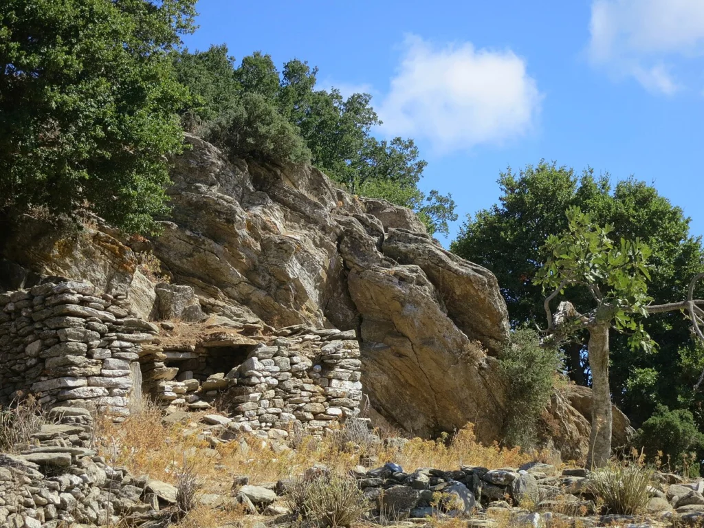 Παλιό πέτρινο μιτάτο βοσκών χτισμένο κάτω από βράχο, ανάμεσα σε δέντρα, πάνω από τη Μονή Φωτοδότη