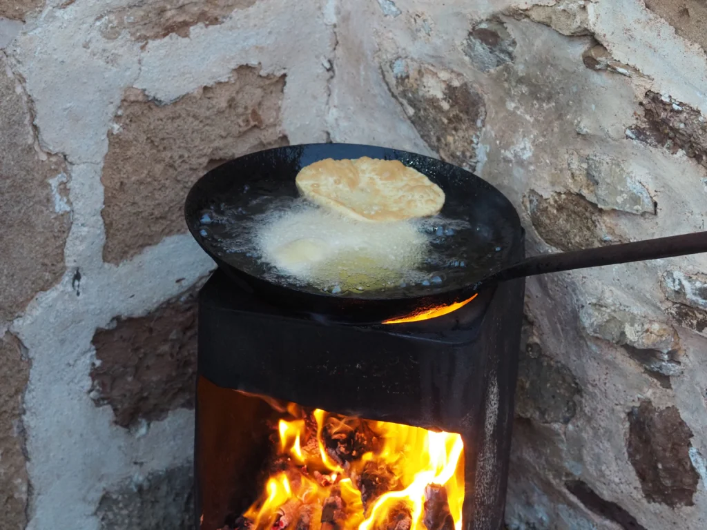 Στρογγυλή πίτα με μυζήθρα τηγανίζεται σε μαύρο τηγάνι πάνω σε μικρή ξυλόσομπα με φωτιά