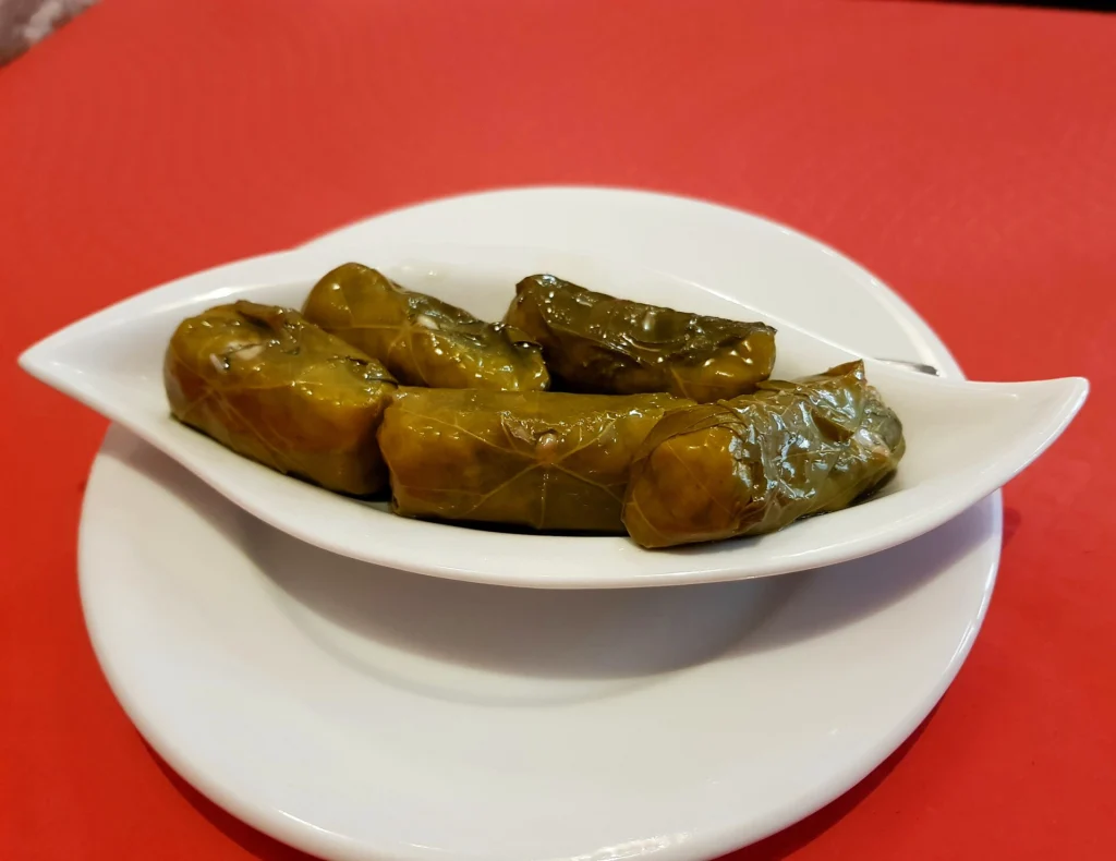 Ντολμαδάκια, γεμιστά φύλλα αμπελιού, σερβιρισμένα σε λευκό πιάτο σχήματος φύλλου