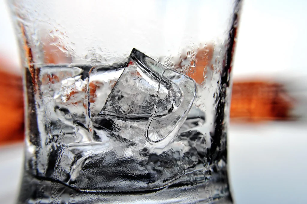 Παγάκια μέσα σε θολό από την υγρασία γυάλινο ποτήρι, σε κοντινό πλάνο με θολό φόντο