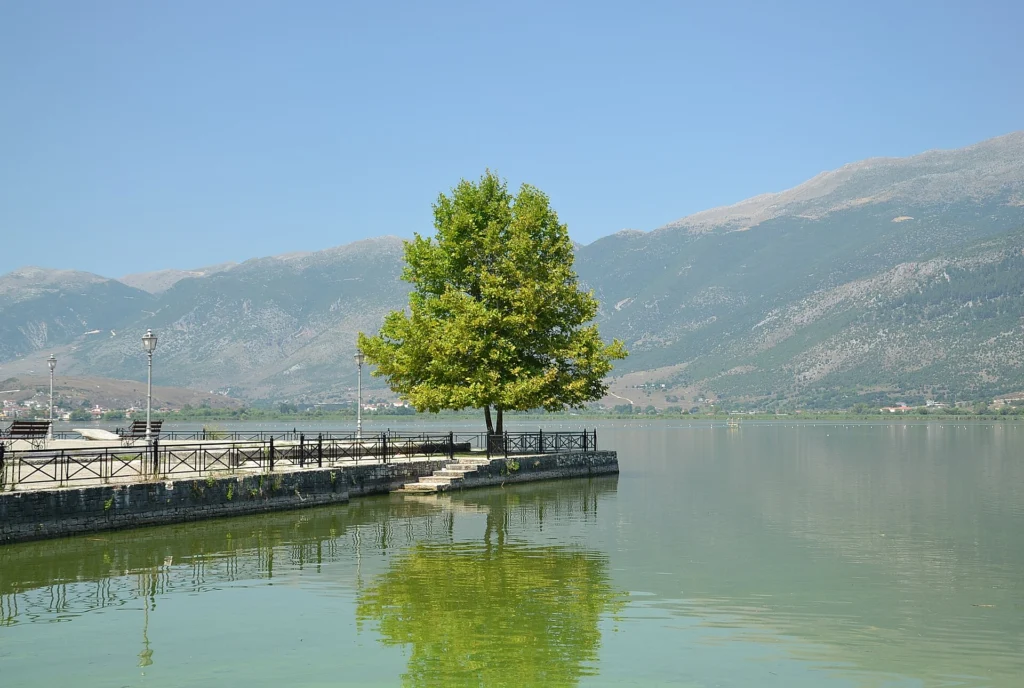 Η λίμνη Παμβώτιδα στα Γιάννενα, με προβλήτα, δέντρο και βουνά στο βάθος