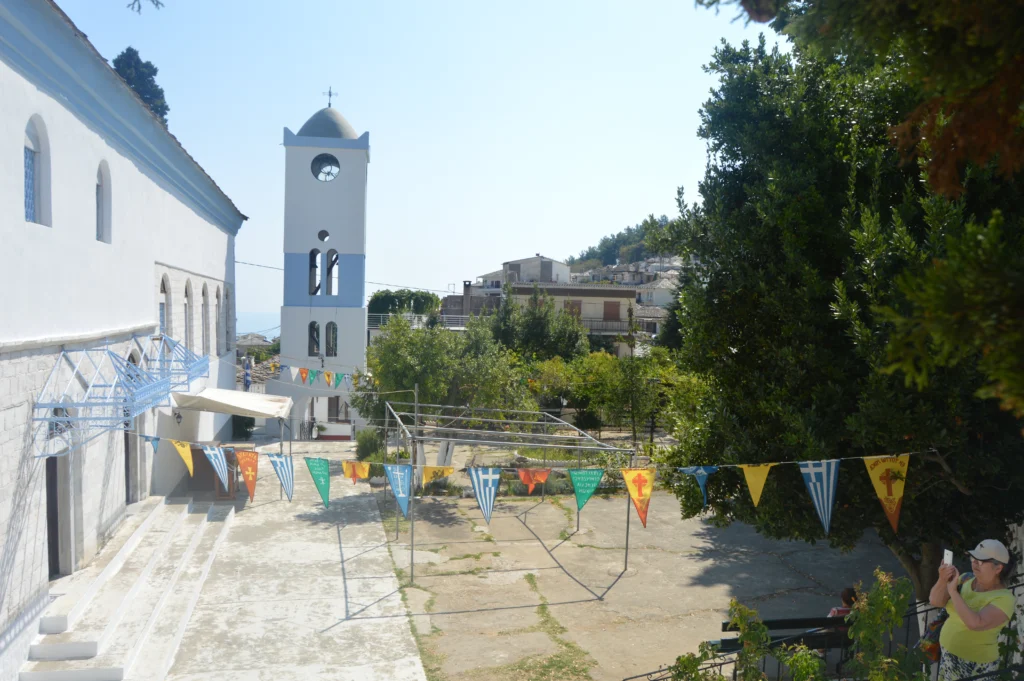 Λευκός ναός με καμπαναριό και πολύχρωμα σημαιάκια στην αυλή, στο χωριό Παναγία της Θάσου