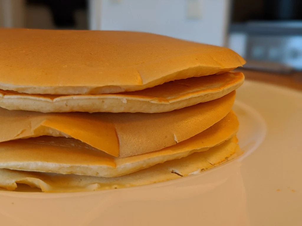 Κοντινή λήψη από το πλάι σε στοίβα pancakes πάνω σε λευκό πιάτο, με θολό φόντο πίσω