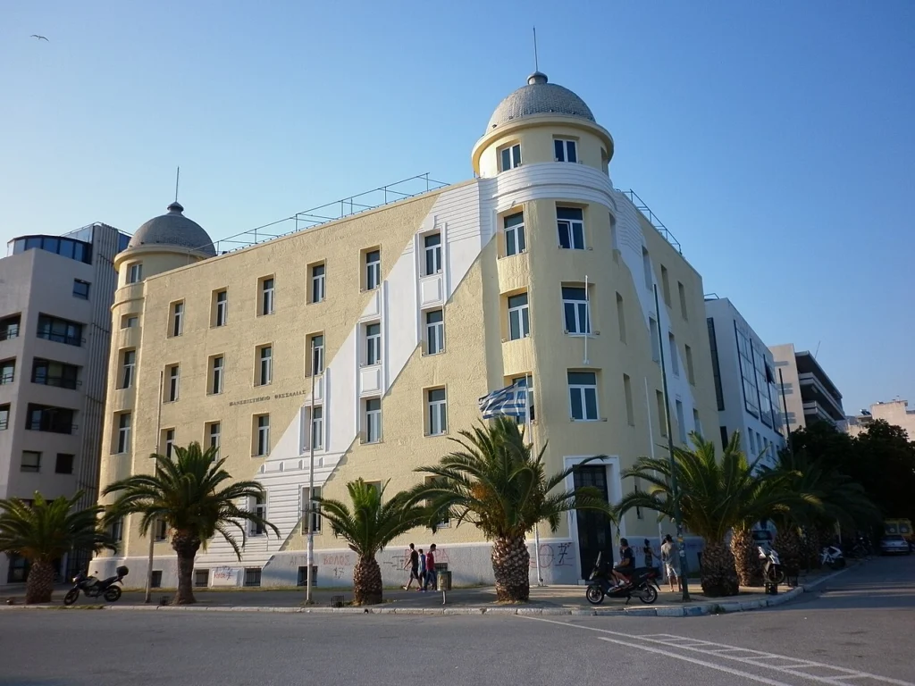 Το κίτρινο κτίριο του Πανεπιστημίου Θεσσαλίας με δύο τρούλους και φοίνικες στην παραλία του Βόλου