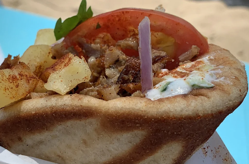 Πίτα γύρο από κοντά με τηγανητές πατάτες, φέτα ντομάτας, ωμό κρεμμύδι και τζατζίκι, ψημένη πίτα