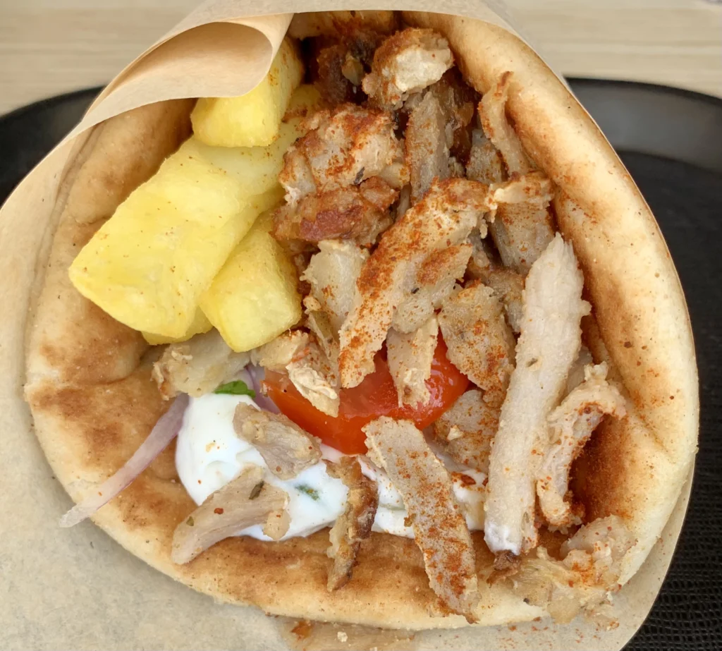 Πίτα τυλιγμένη σε χαρτί με γύρο, πατάτες τηγανητές, ντομάτα, κρεμμύδι και λευκή σάλτσα
