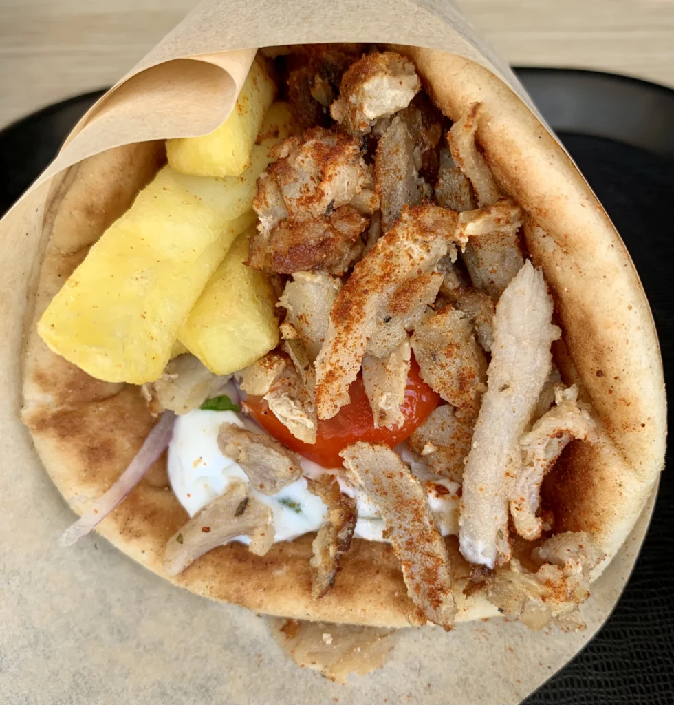 Πίτα γύρο από ψηλά με φέτες γύρου, χοντρές πατάτες, ντομάτα, κρεμμύδι και τζατζίκι, τυλιγμένη σε χαρτί