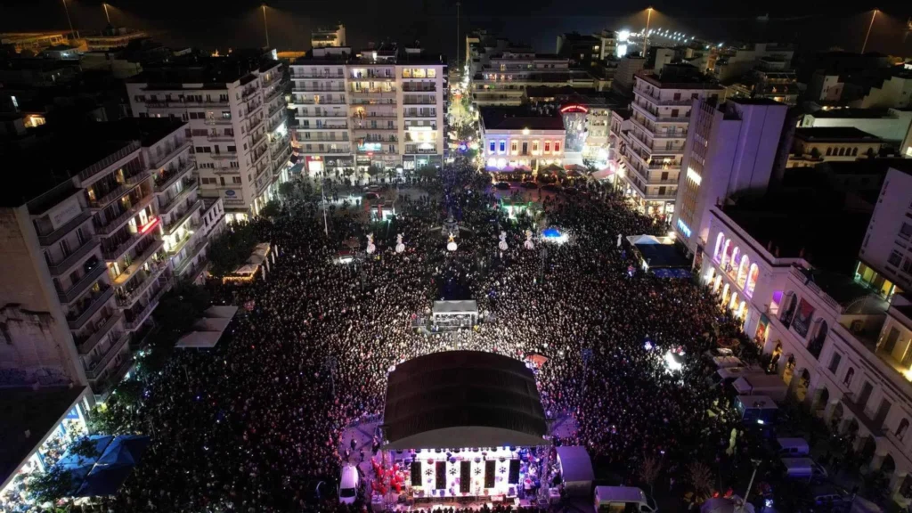 Αεροφωτογραφία της φωτισμένης πλατείας Γεωργίου Α΄ στην Πάτρα, γεμάτης κόσμο, με σκηνή στο κέντρο, βράδυ