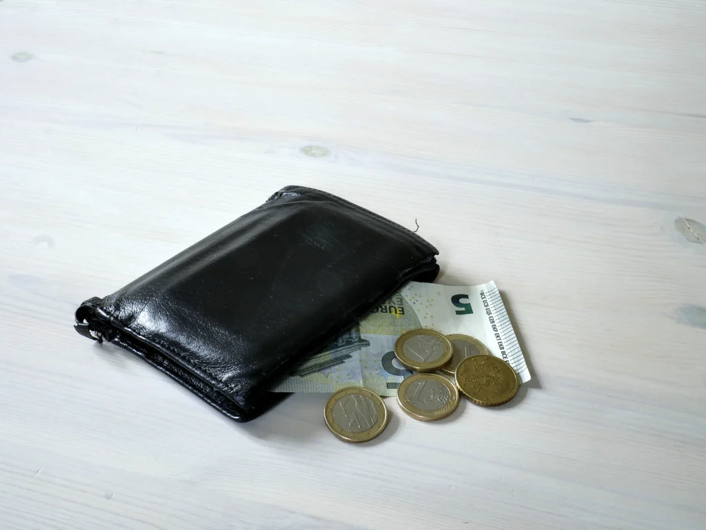 Μαύρο πορτοφόλι με χαρτονόμισμα των 5 ευρώ και κέρματα πάνω σε ανοιχτόχρωμο ξύλινο τραπέζι