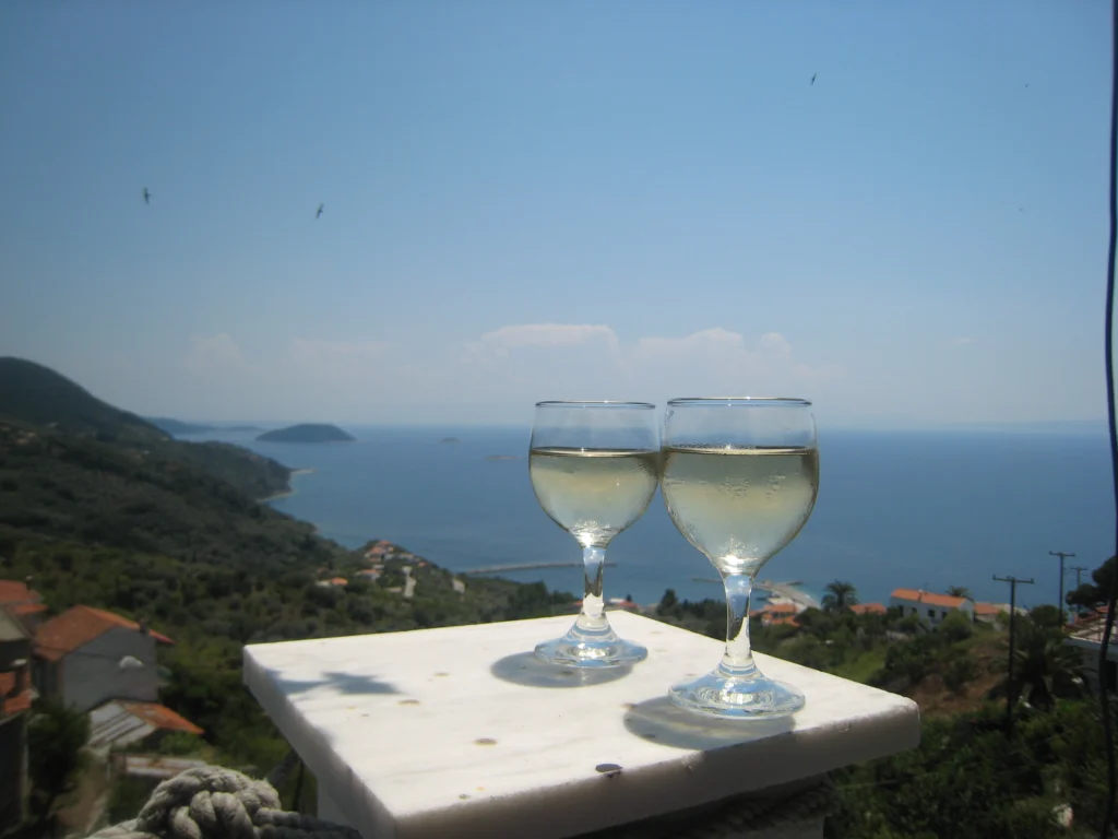 Δύο ποτήρια ρετσίνα σε μαρμάρινο τραπέζι, με φόντο θάλασσα, νησάκια και πράσινη πλαγιά