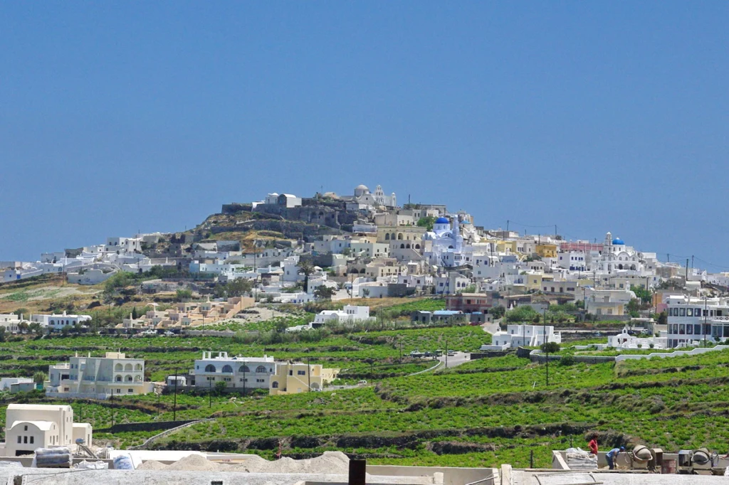 Το χωριό Πύργος της Σαντορίνης με λευκά σπίτια σε λόφο και πράσινα αμπέλια σε αναβαθμίδες γύρω του