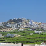 Το χωριό Πύργος της Σαντορίνης με λευκά σπίτια σε λόφο και πράσινα αμπέλια σε αναβαθμίδες γύρω του