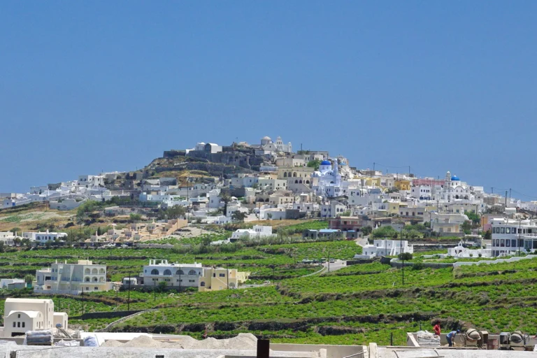 Το χωριό Πύργος της Σαντορίνης με λευκά σπίτια σε λόφο και πράσινα αμπέλια σε αναβαθμίδες γύρω του
