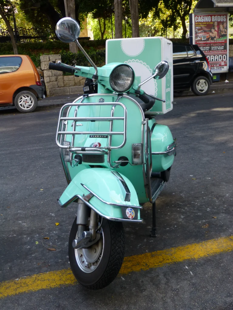 Πράσινο σκούτερ Piaggio με κουτί διανομής φαγητού πίσω από τη σέλα, σταθμευμένο σε δρόμο της Ρόδου