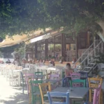 Τραπέζια και καρέκλες ταβέρνας κάτω από δέντρο δίπλα στη θάλασσα στον Τόλο της Πελοποννήσου