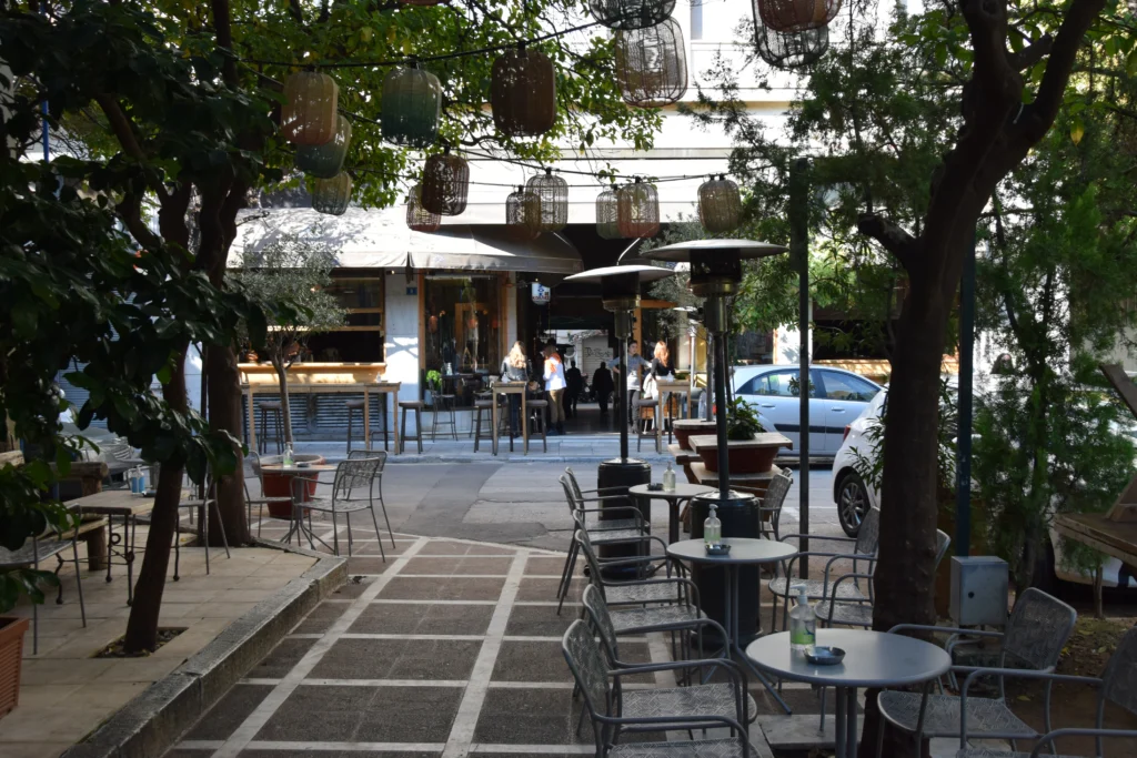 Άδεια τραπεζάκια και καρέκλες με θερμάστρες και φανάρια κάτω από δέντρα σε πεζόδρομο της Αθήνας