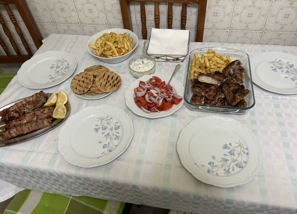Τραπέζι με χοιρινά καλαμάκια, ψητό κοτόπουλο, ψημένες πίτες, πατάτες, τζατζίκι και σαλάτα ντομάτα με κρεμμύδι