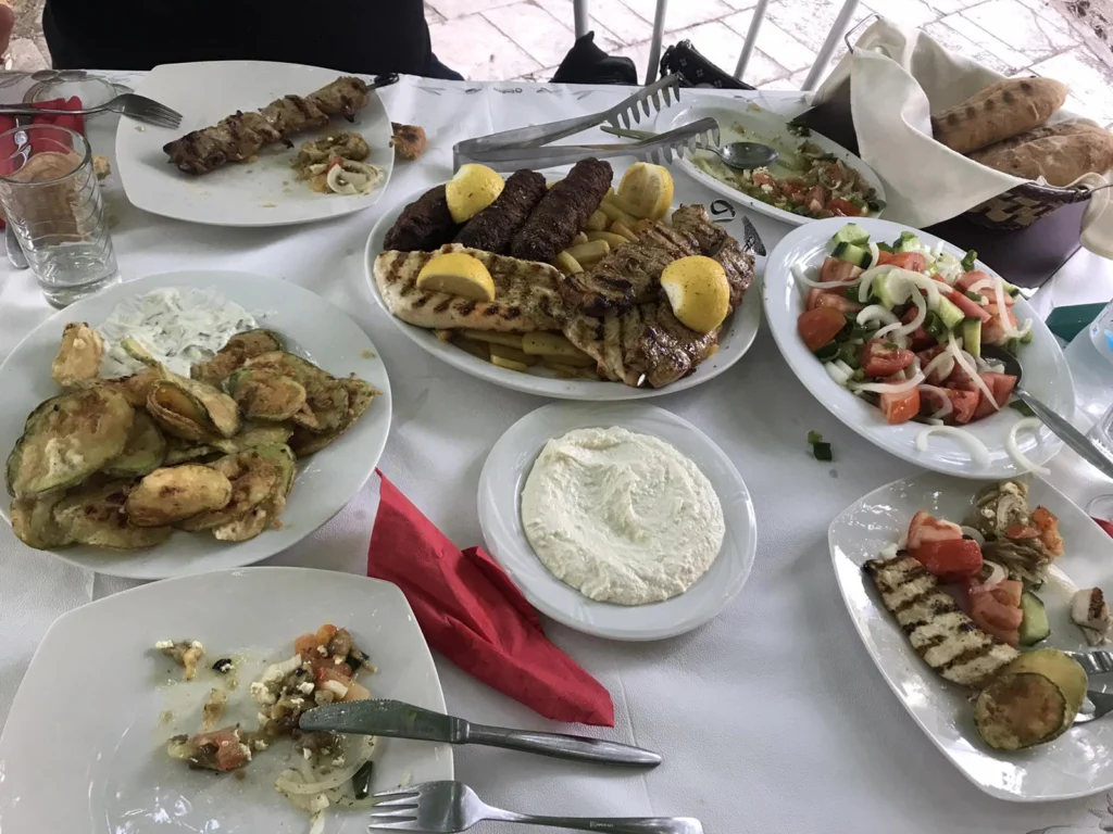 Τραπέζι ταβέρνας με σουβλάκι, μπιφτέκια, χωριάτικη, τζατζίκι και ψητά λαχανικά σε λευκά πιάτα