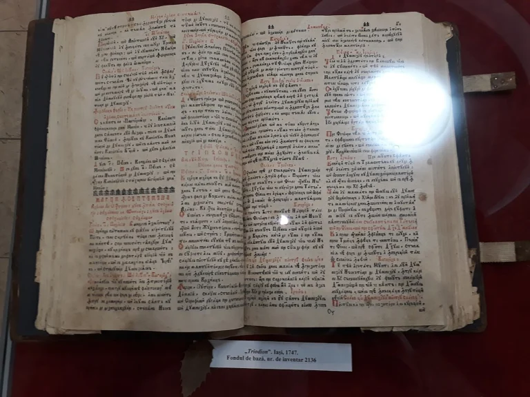 Ανοιχτό παλιό έντυπο βιβλίο Τριωδίου του 1747 με κόκκινα και μαύρα γράμματα, σε προθήκη μουσείου