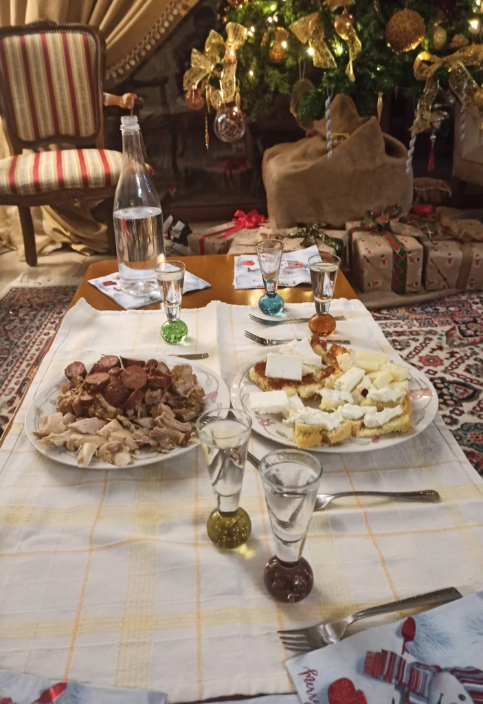 Ποτηράκια τσίπουρο, μπουκάλι νερό, πιάτο με λουκάνικο και κρέας και πιάτο με τυριά πάνω σε κομμάτια ψημένης ζύμης