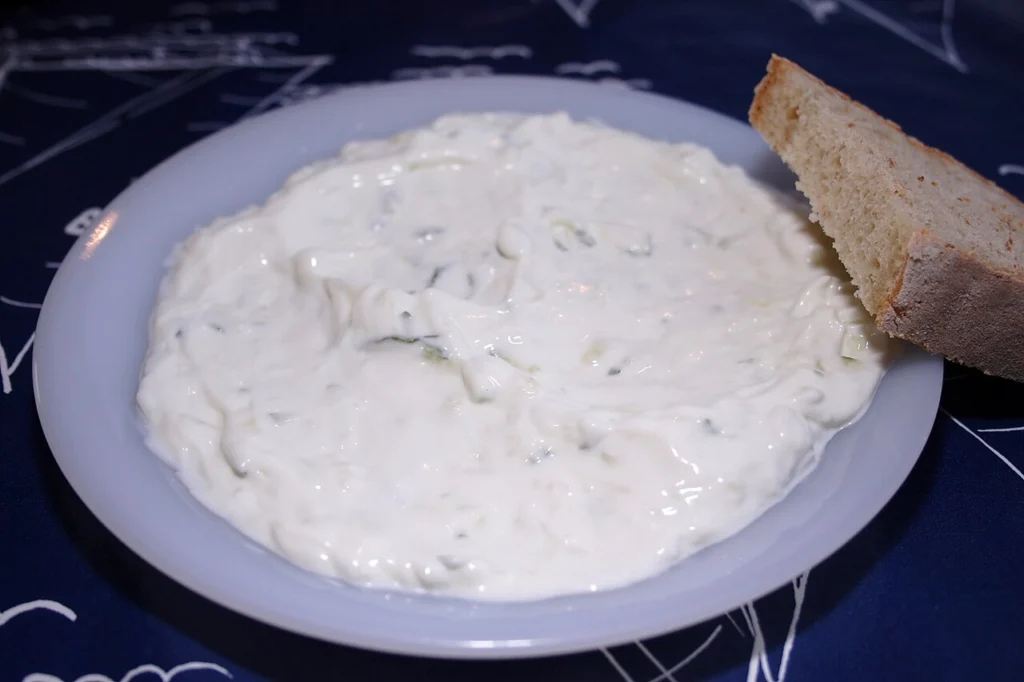 Πιάτο με τζατζίκι και μια φέτα ψωμί στο πλάι, πάνω σε σκούρο μπλε τραπεζομάντιλο