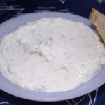 Πιάτο με τζατζίκι και μια φέτα ψωμί στο πλάι, πάνω σε σκούρο μπλε τραπεζομάντιλο