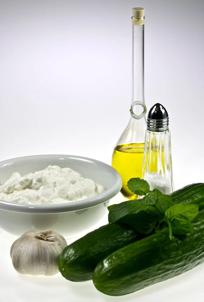 Γιαούρτι σε μπολ, δύο αγγούρια, σκόρδο, δυόσμος, ελαιόλαδο και αλατιέρα, τα υλικά του τζατζικιού